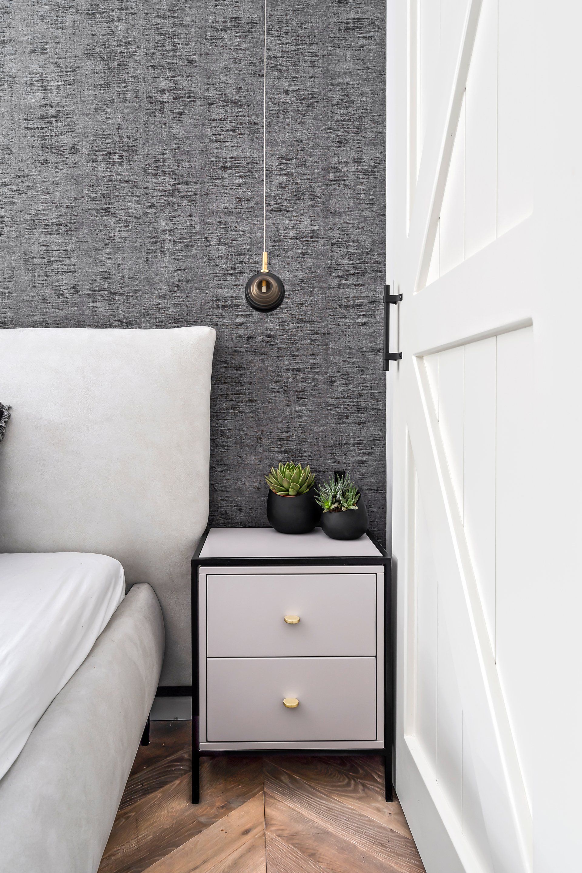 מיטה זוגית וברקע טפט אפור עם גוף תאורה יורד מהתקרה