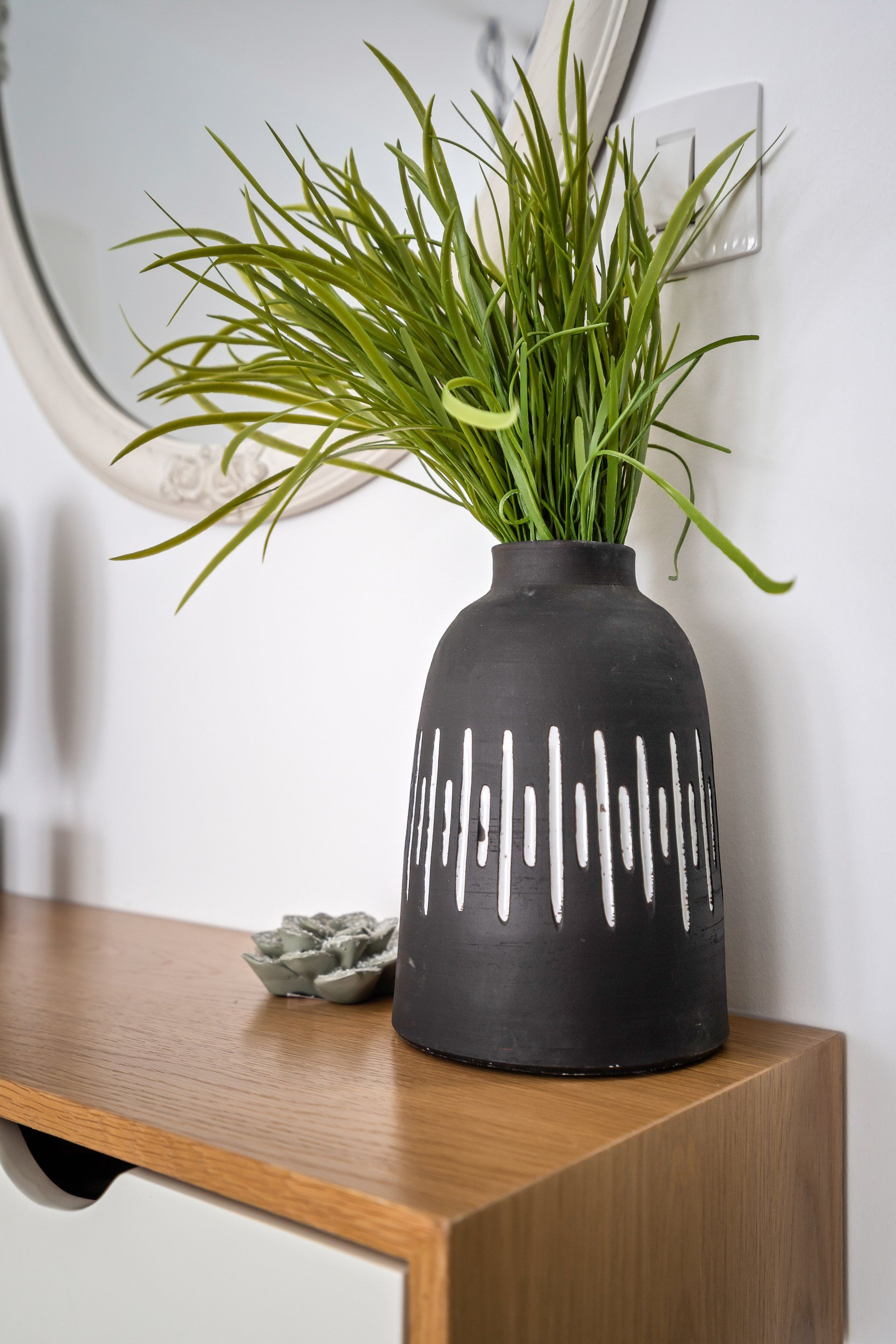 אגרטל שחור מקרמיקה עם צמחי נוי מעל קונסולה