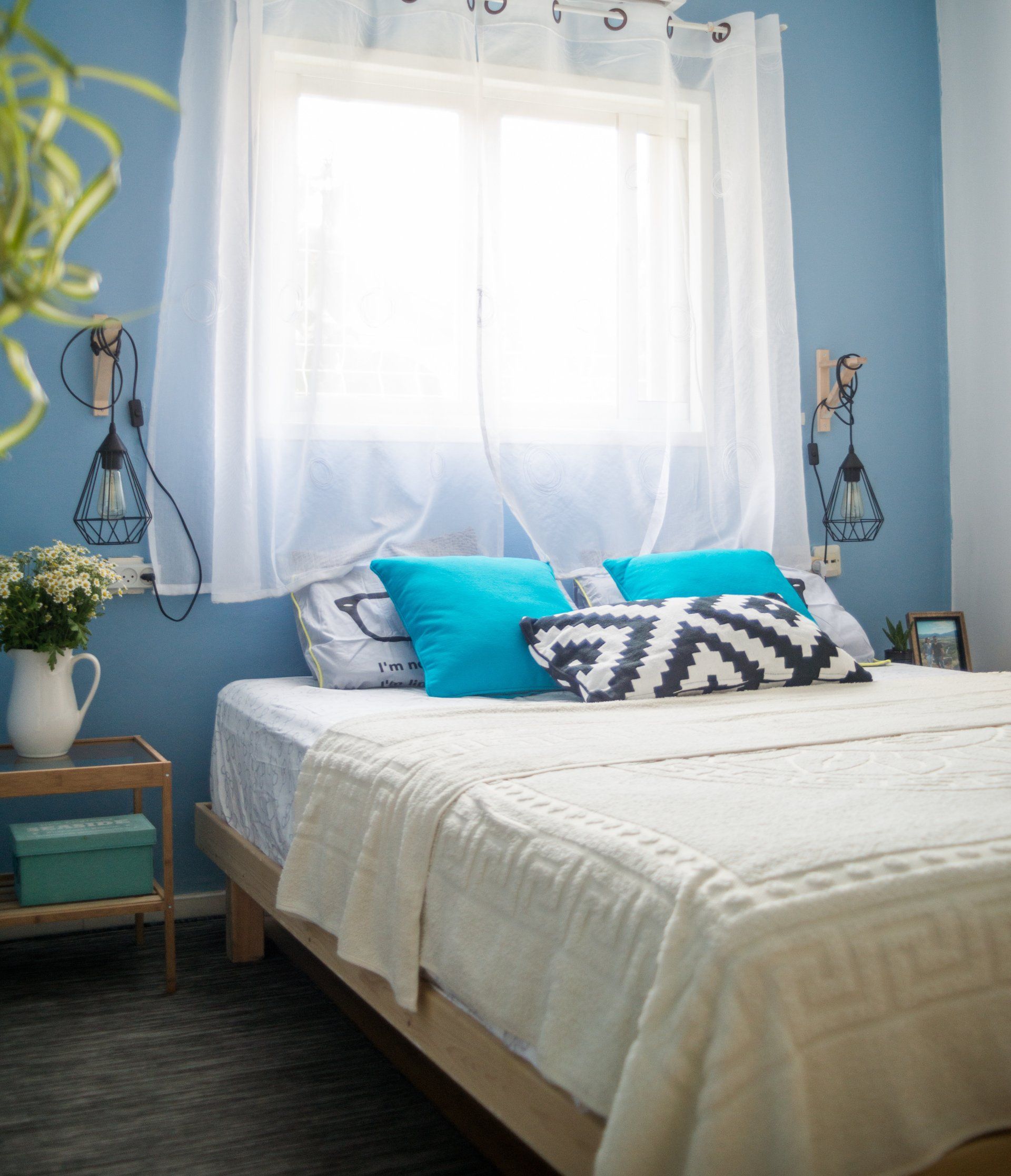חדר שינה עם מיטה ומצעים לבנים כריות כחולות טורקיז וקיר בצבע כחול