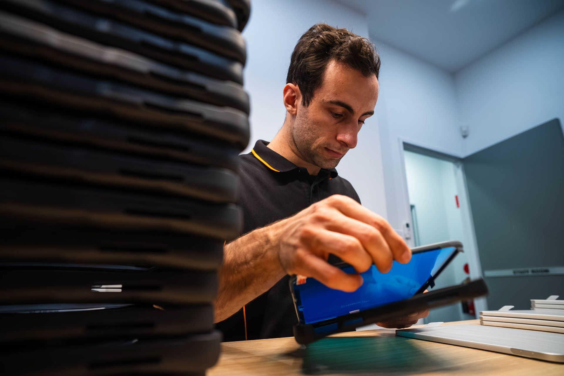 Man scanning a blue tablet at a workbench beside a stack of black trays