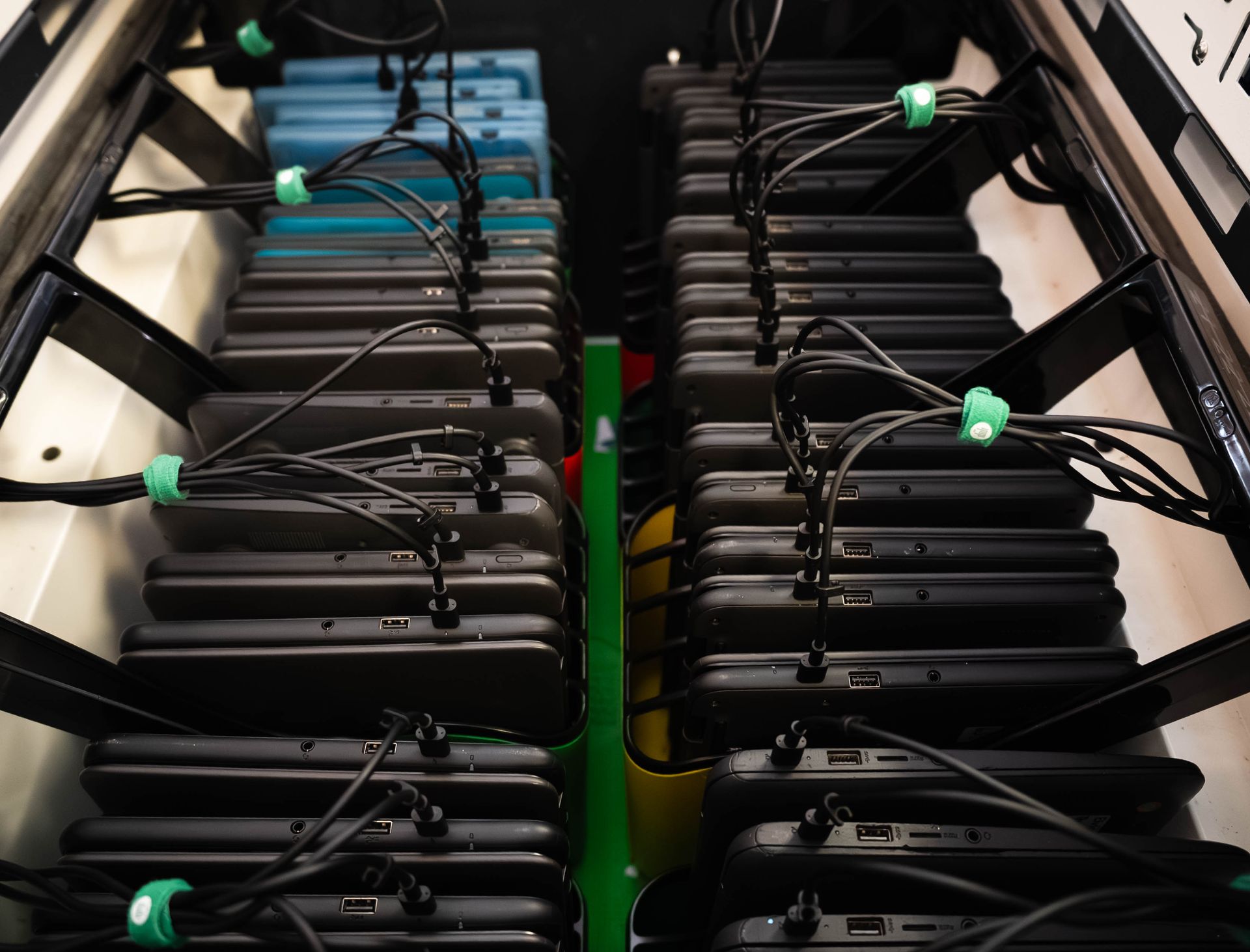 Rows of black laptop-like devices with cables and green connectors inside a server rack