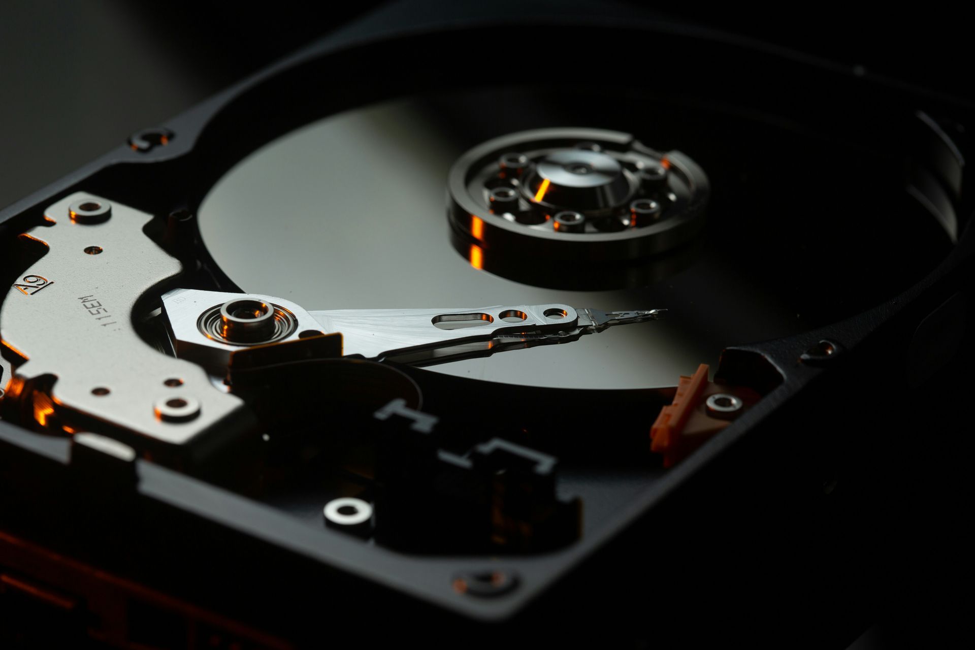 Close-up of an open hard drive platter and actuator arm in dim light