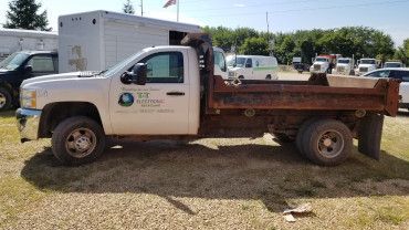 A side view of a white commercial dump truck parked on a gravel lot under a clear blue sky.