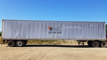 White semi-trailer parked on a dirt lot under a clear blue sky, featuring 
