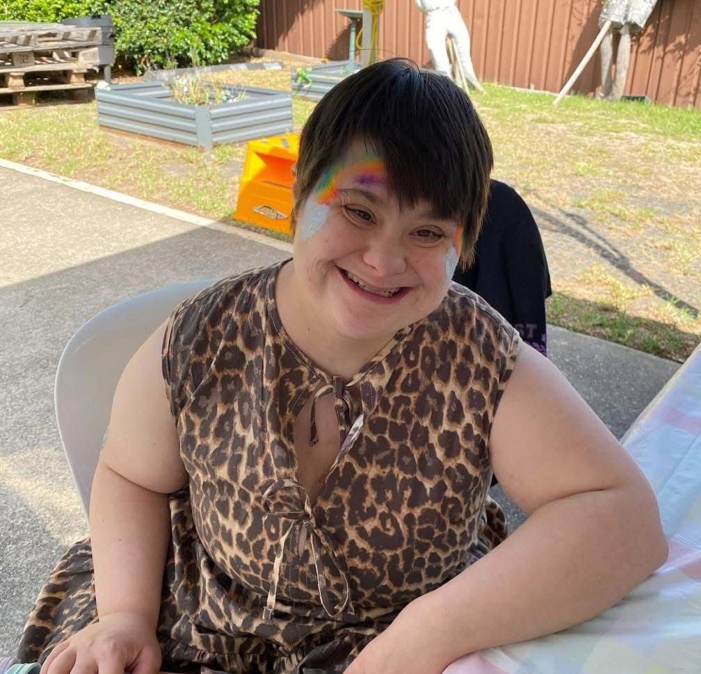 NDIS Support Coordination. A woman in a leopard print dress has a rainbow painted on her face.
