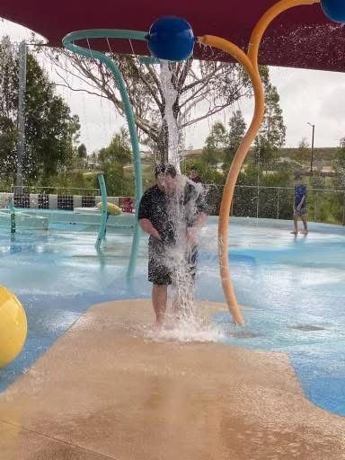 A man is standing under a water fountain at a water park.