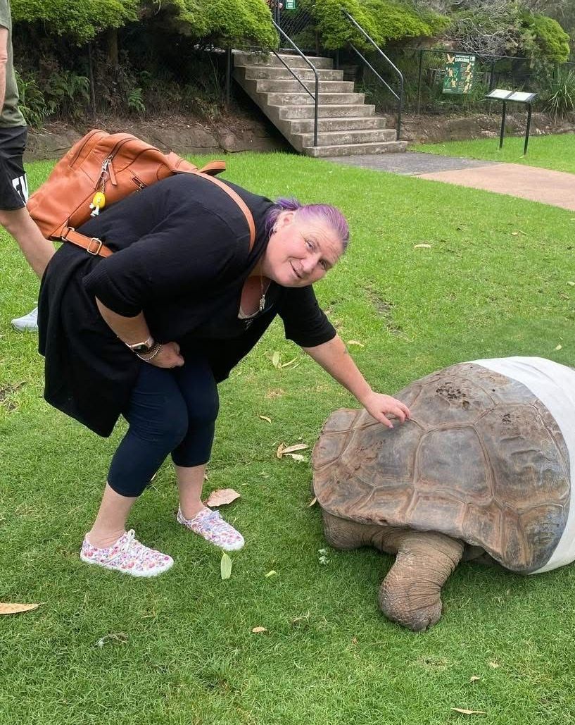 Social and Community outings. A woman is petting a large turtle in a park.