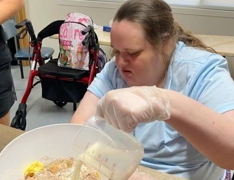 A woman is pouring milk into a bowl of food.