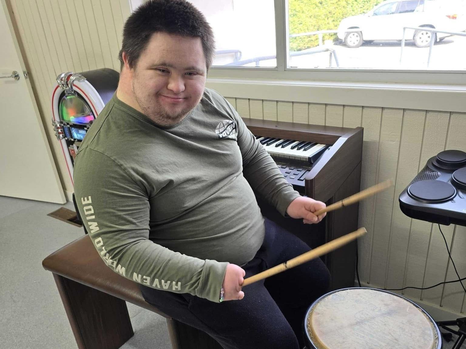 Centre based day programs. A man is sitting in a chair playing drums.