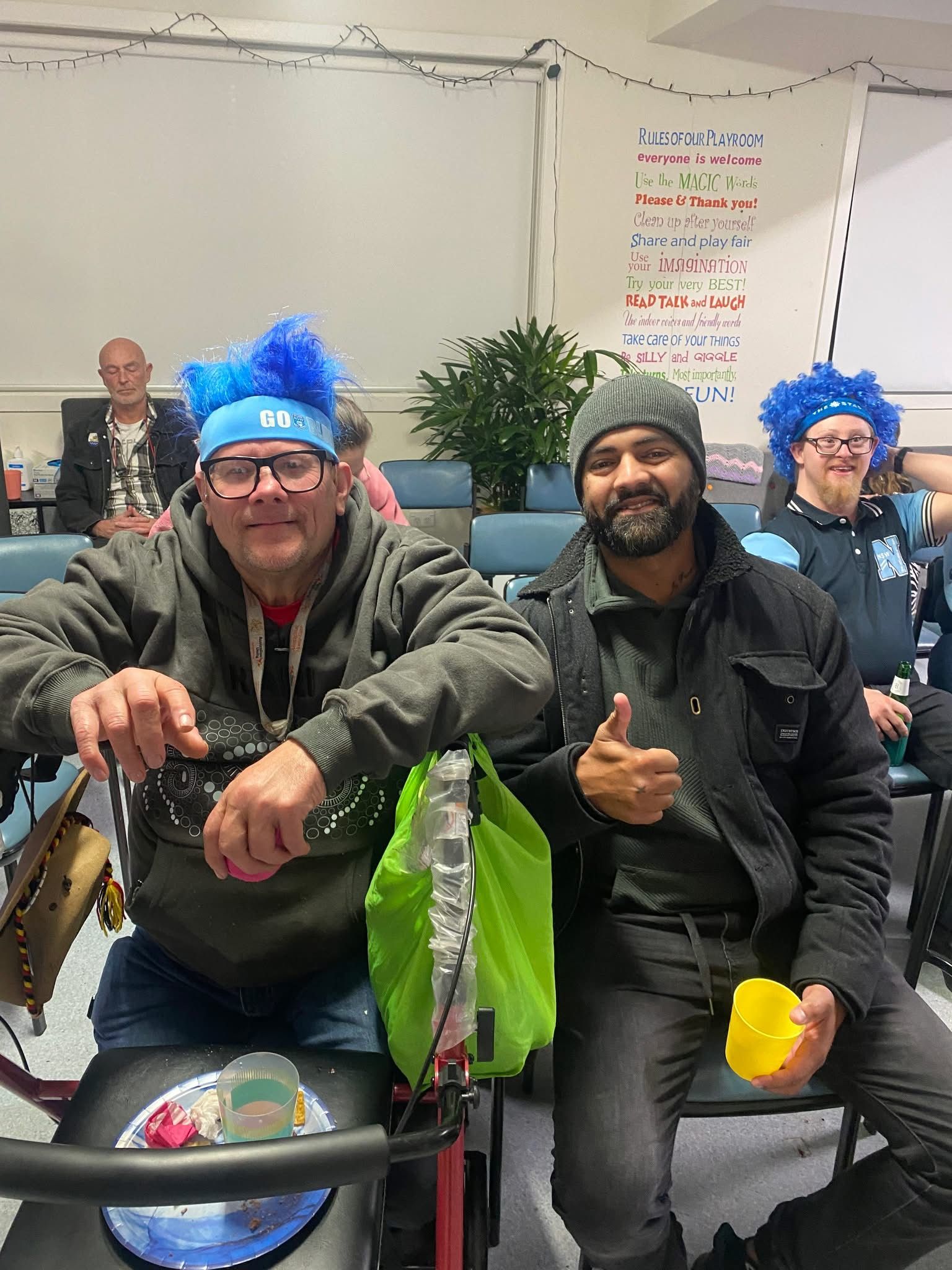 Two men wearing blue wigs are sitting next to each other on a bicycle.