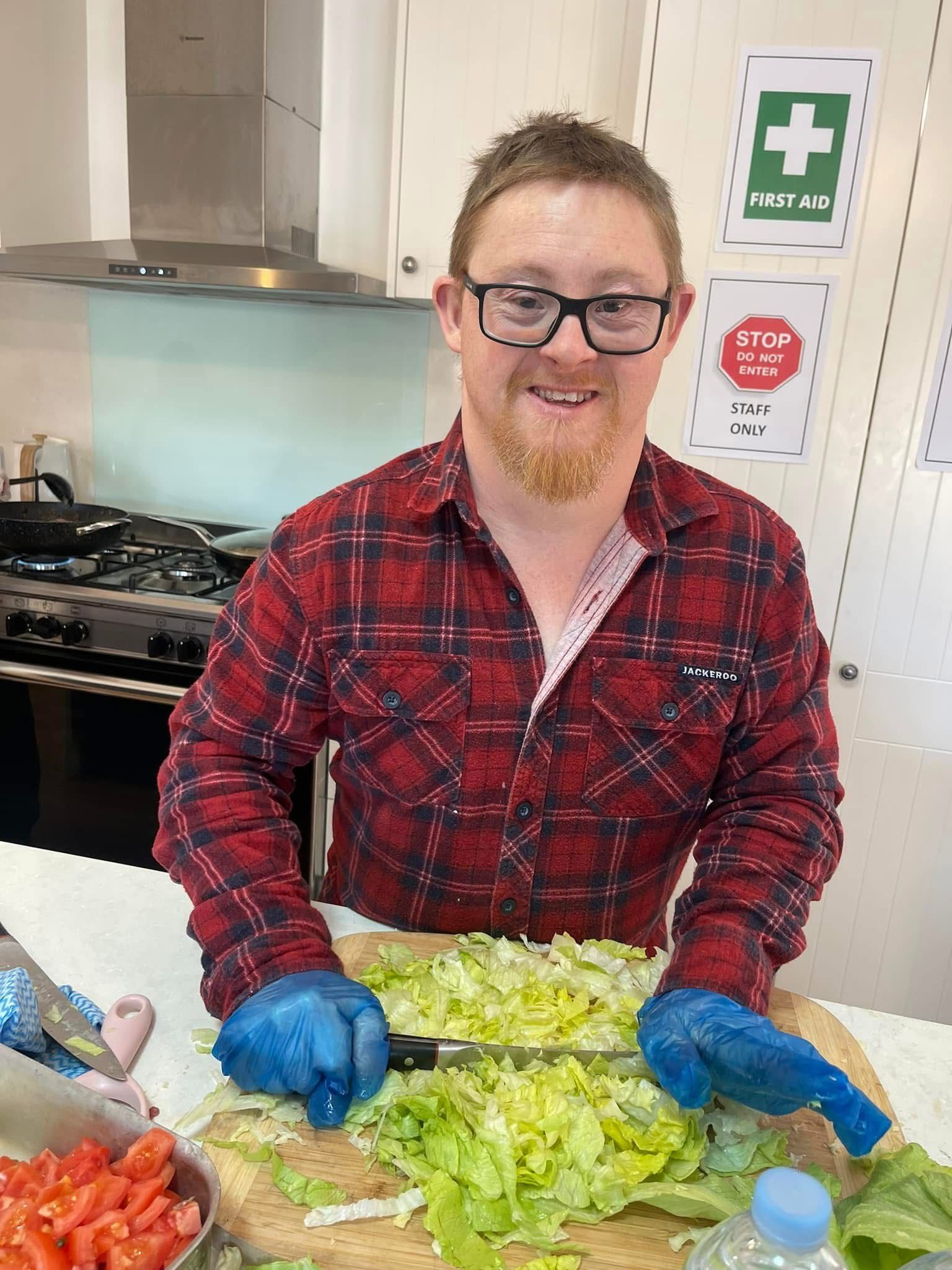 Daily living skills. A man is cutting lettuce on a cutting board in a kitchen.