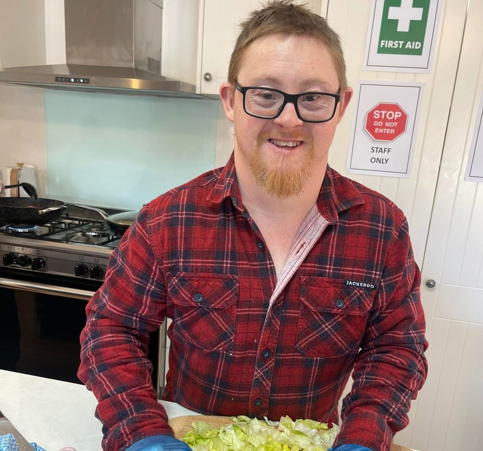 Daily activities, learning how to cook. A man in a plaid shirt is cutting lettuce in a kitchen.
