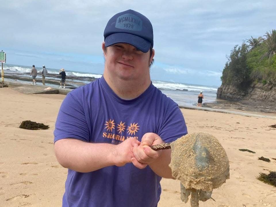 Social fishing trips. A man in a purple shirt is holding a jellyfish on the beach.