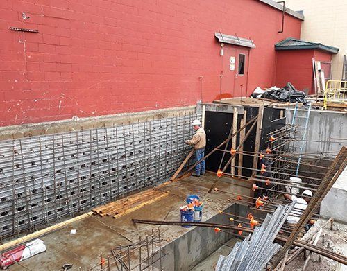 a man is working on a concrete wall in front of a red building
