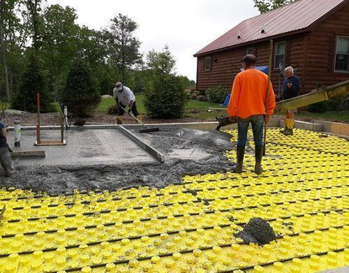 a group of men are working on a concrete floor in front of a log cabin