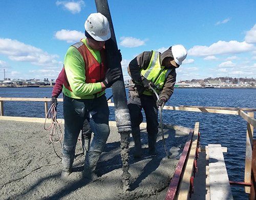 two construction workers are working on a dock next to a body of water