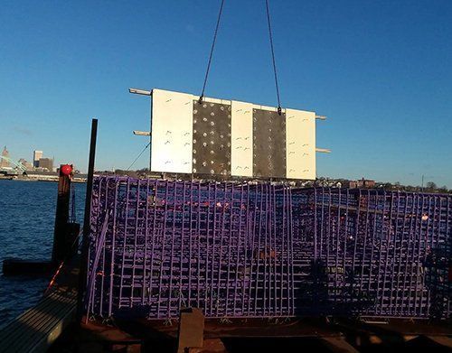 a large purple cage is being lifted by a crane over a body of water