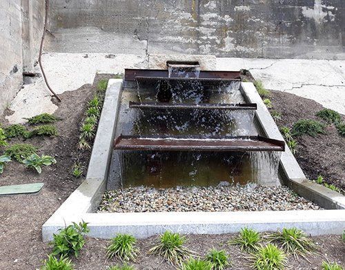 a waterfall is surrounded by gravel and plants in a garden