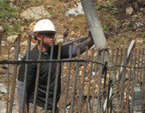 a man wearing a hard hat and sunglasses is standing behind a fence