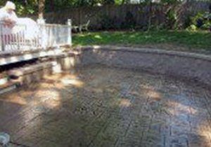 a person is standing on a concrete patio next to a pool