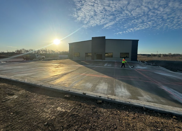 A man is walking down a concrete driveway in front of a building under construction.