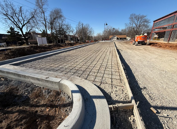 A concrete parking area is being installed on a dirt road
