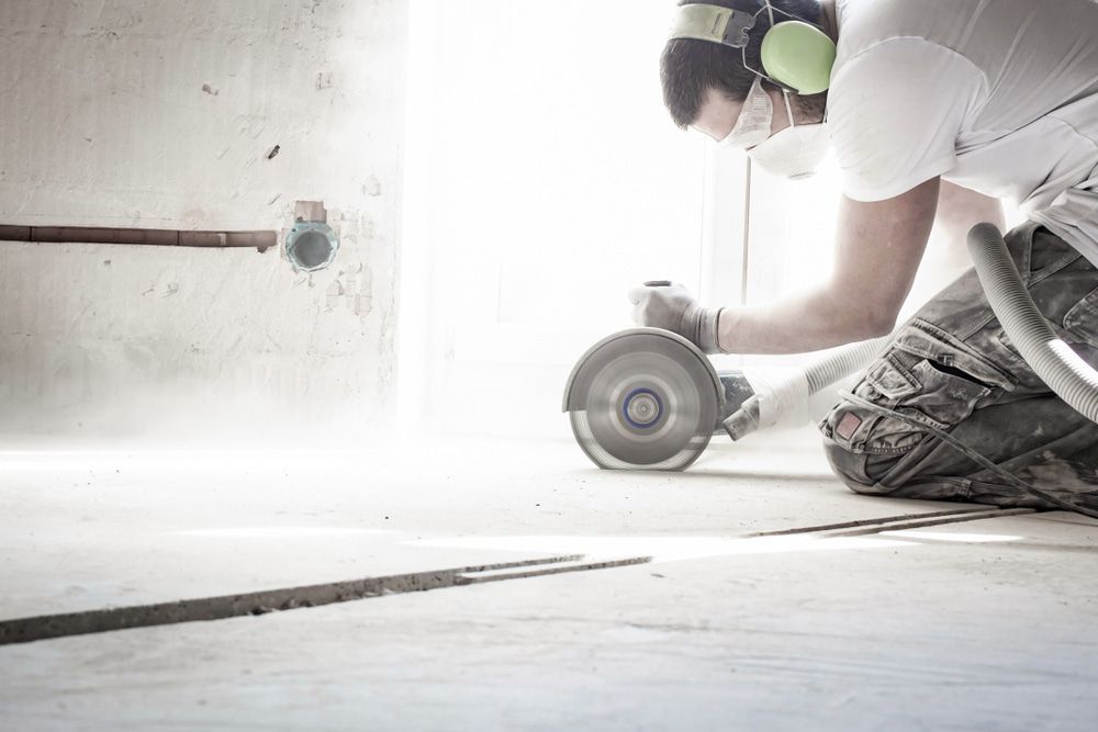 A Man Is Cutting A Hole In The Floor With A Grinder — Pro Cut N Core In Cairns, QLD