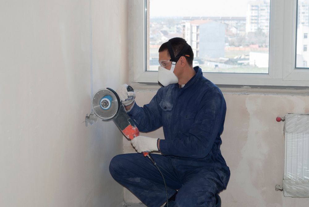 A Man Wearing A Mask Is Using A Grinder To Cut A Hole In A Wall — Pro Cut N Core In Manunda, QLD
