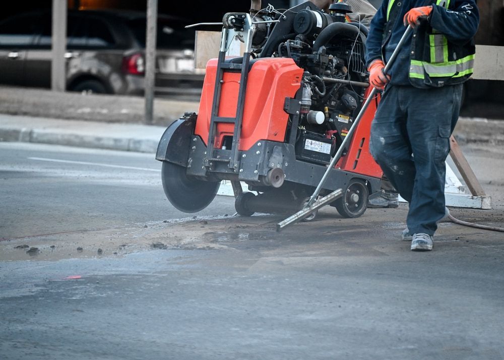 A Man Is Using A Concrete Saw To Cut A Road — Pro Cut N Core In Manunda, QLD