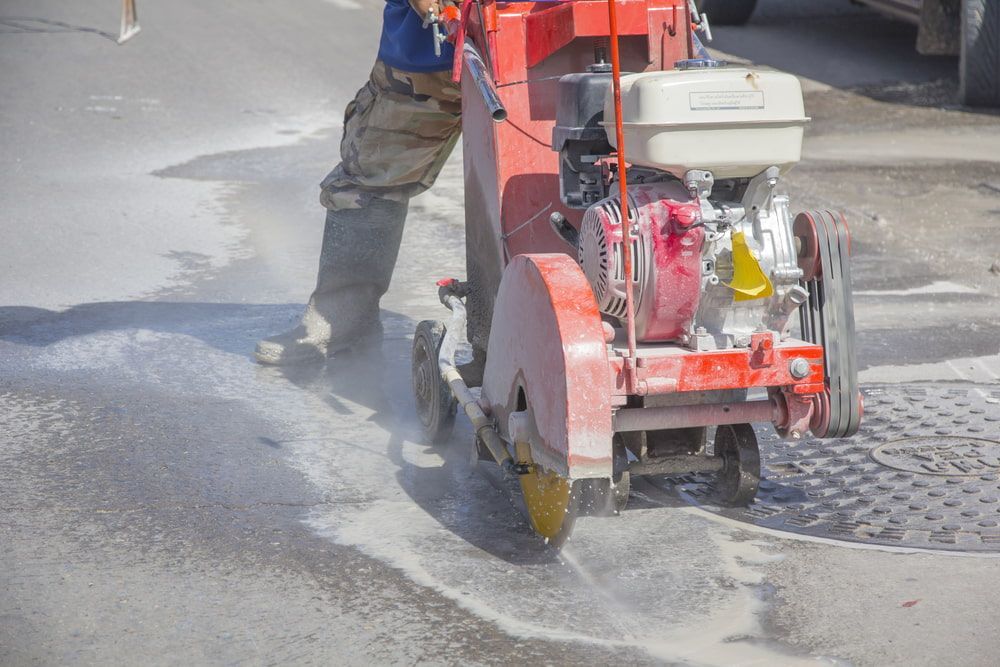 A Man Is Using A Concrete Saw To Cut A Manhole Cover — Pro Cut N Core In Mareeba, QLD