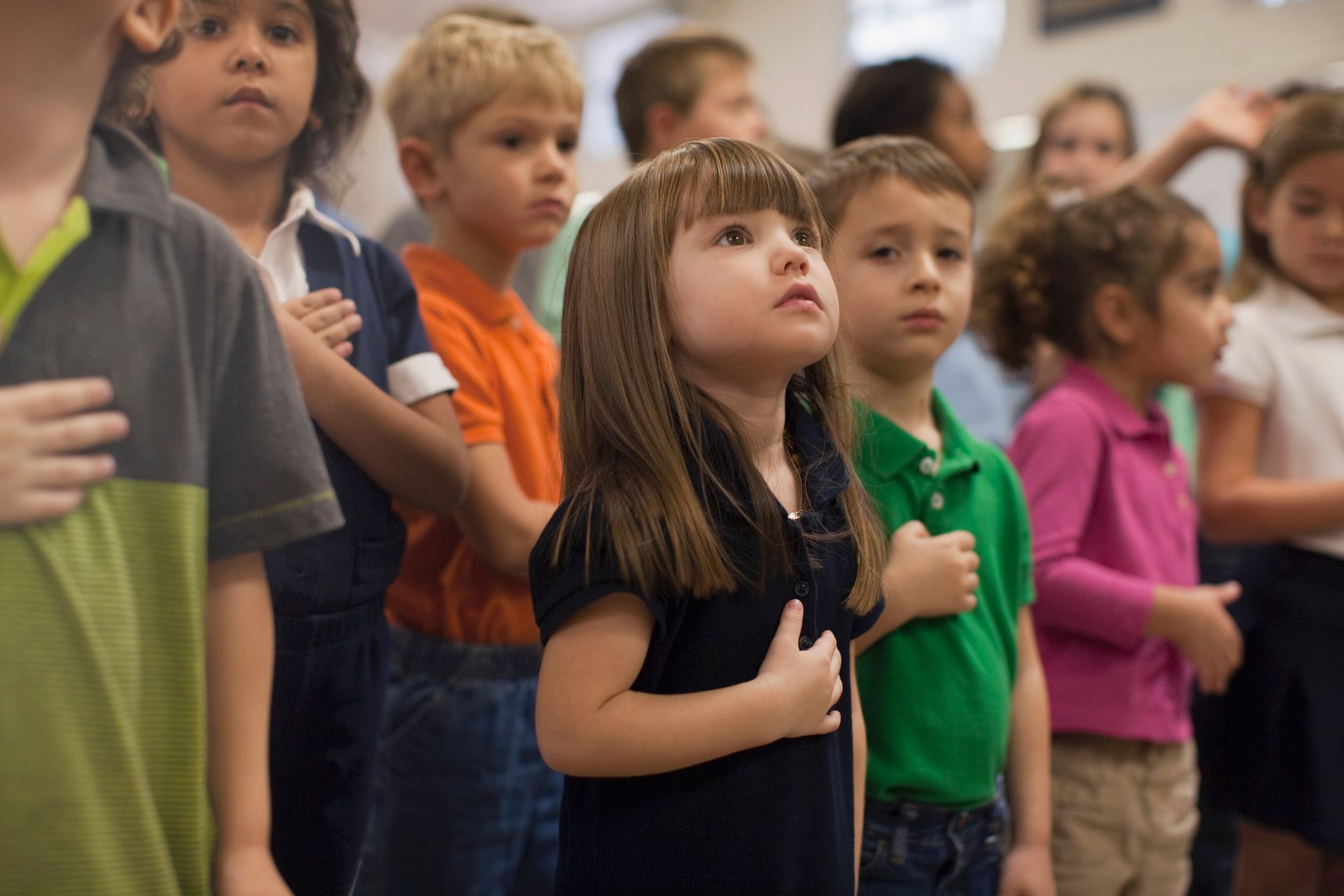 Children with hands over hearts, reciting the Pledge of Allegiance in a school setting.