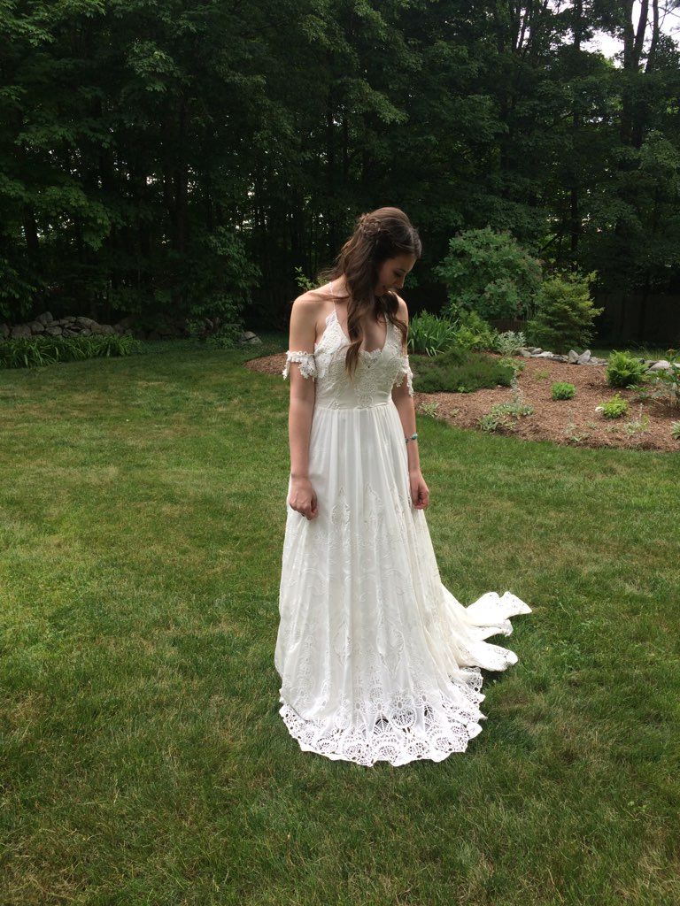 A woman in a white wedding dress is standing in the grass.