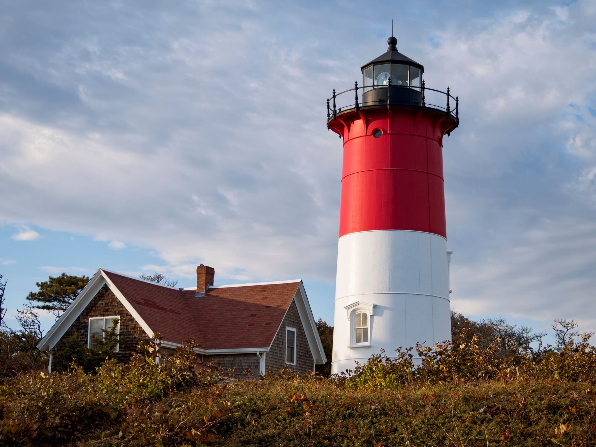 A red and white lighthouse with a house in the background