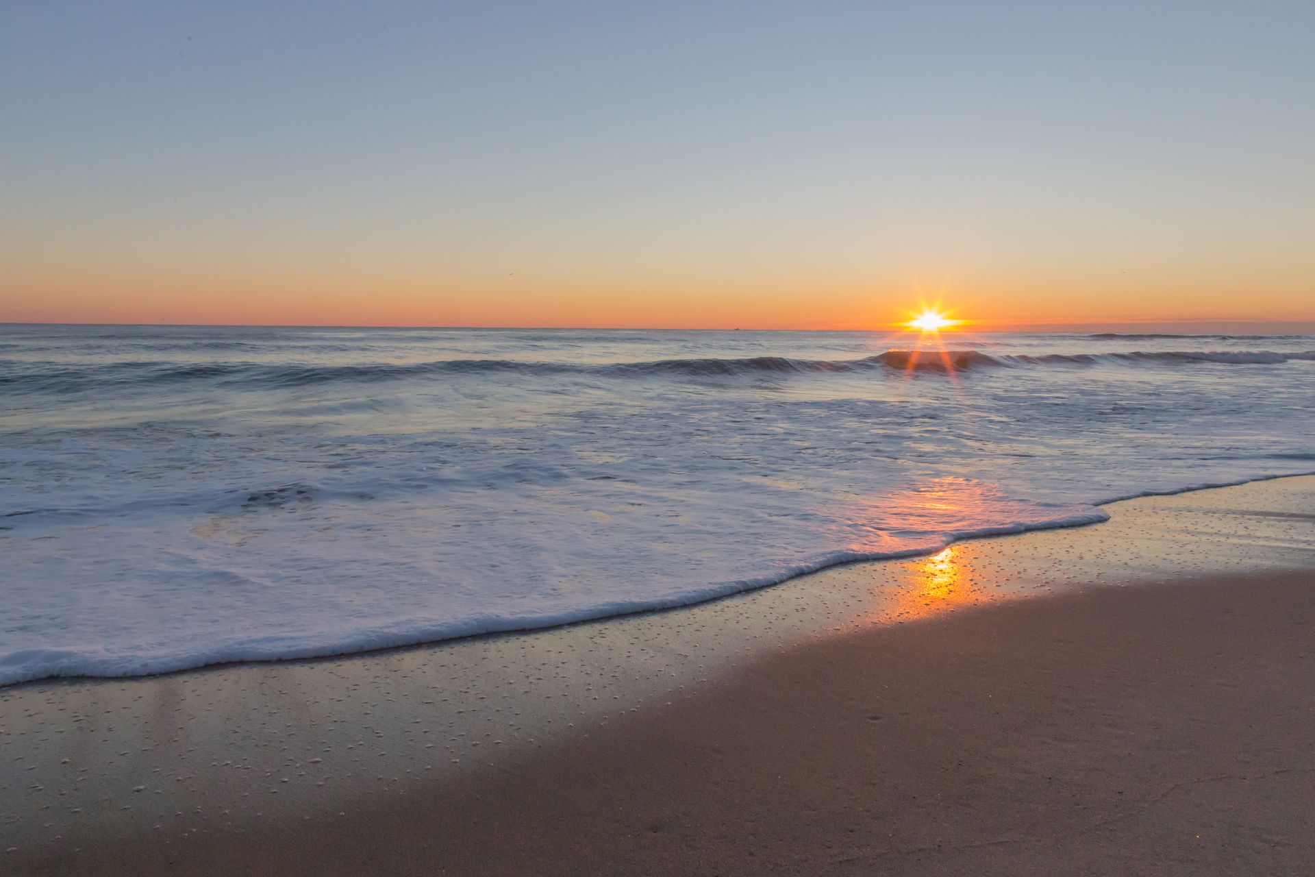 The sun is setting over the ocean on a beach.