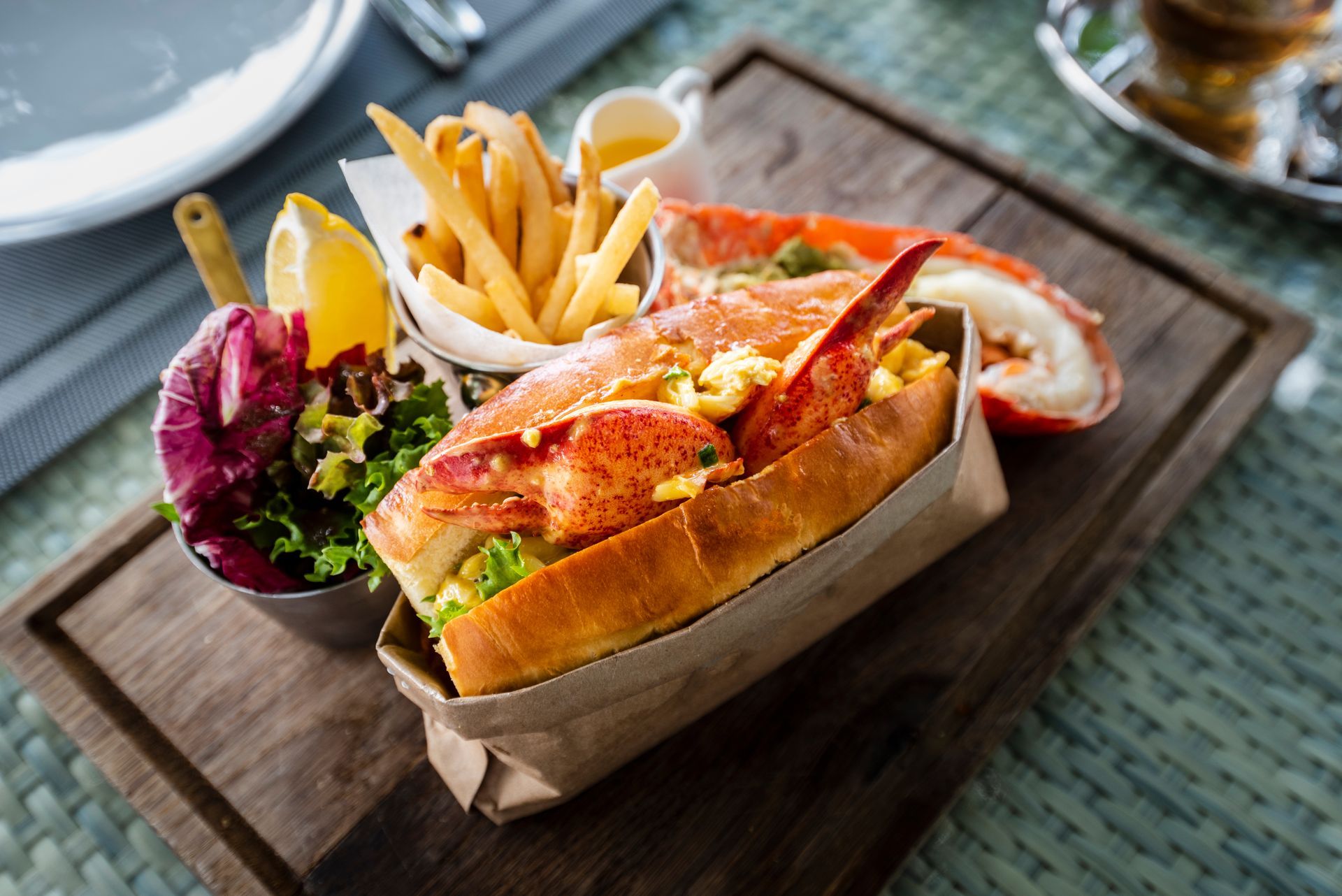 A lobster roll with french fries and a salad on a wooden cutting board.