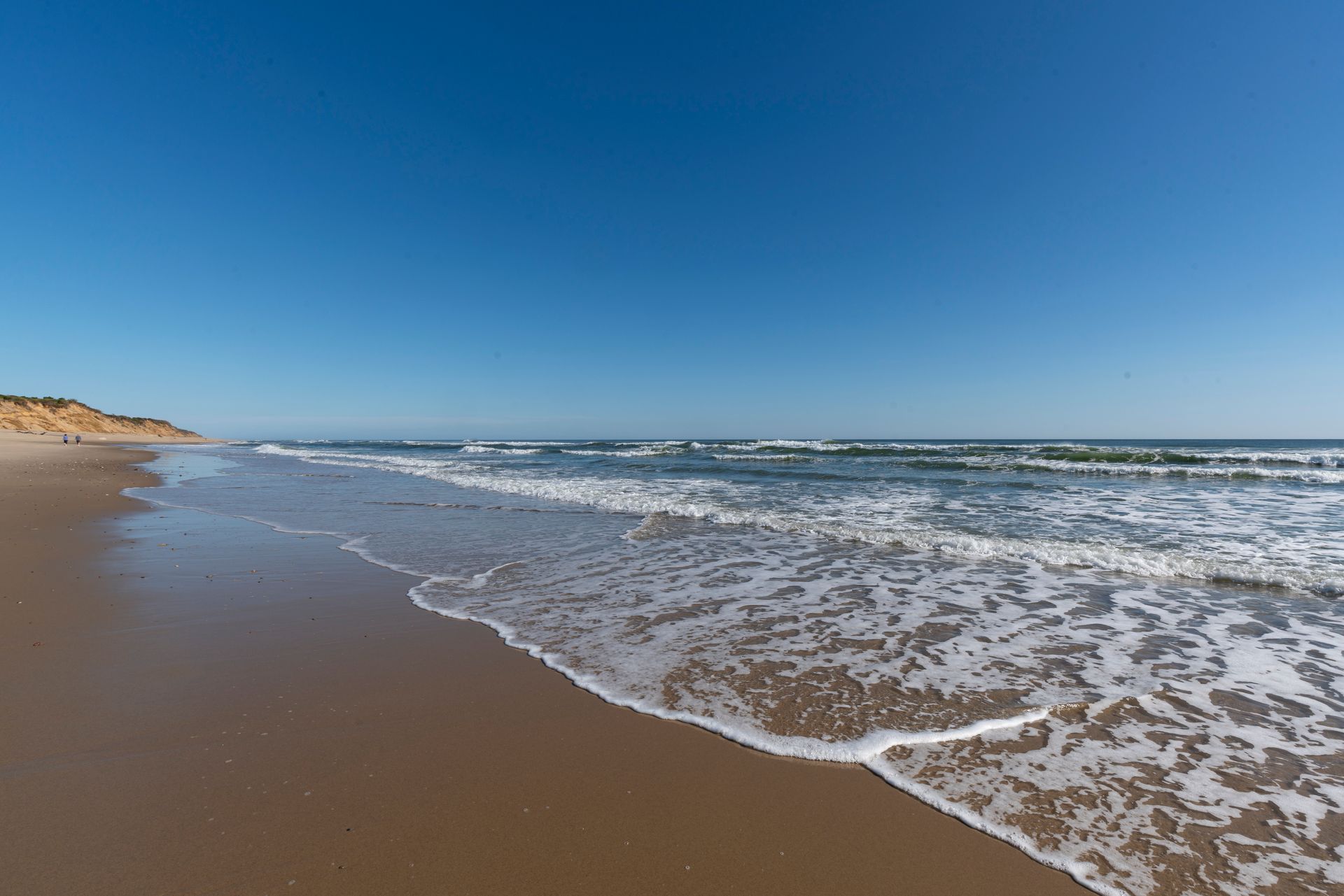 A beach with waves crashing on the sand on a sunny day.