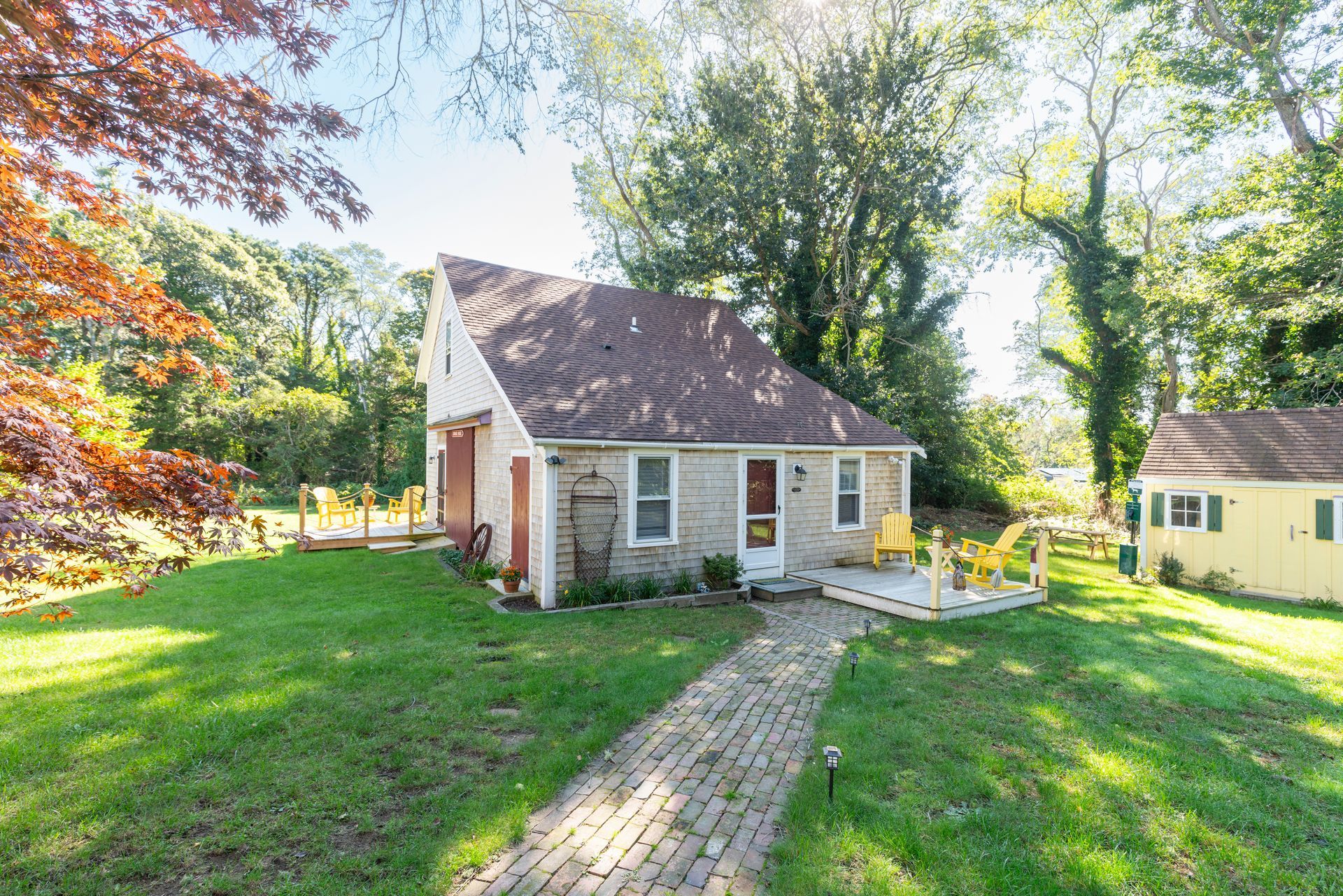 A small house with a brick walkway leading to it is surrounded by trees and grass.