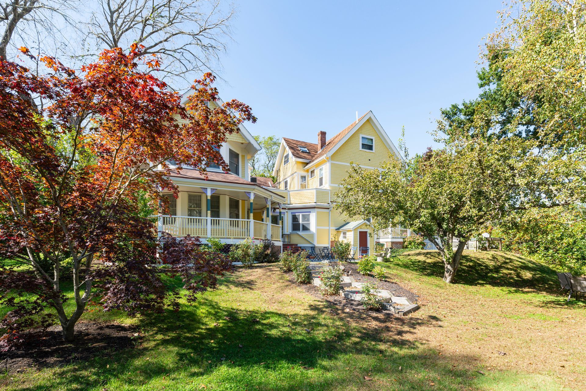 A large yellow house is surrounded by trees and grass on a sunny day.