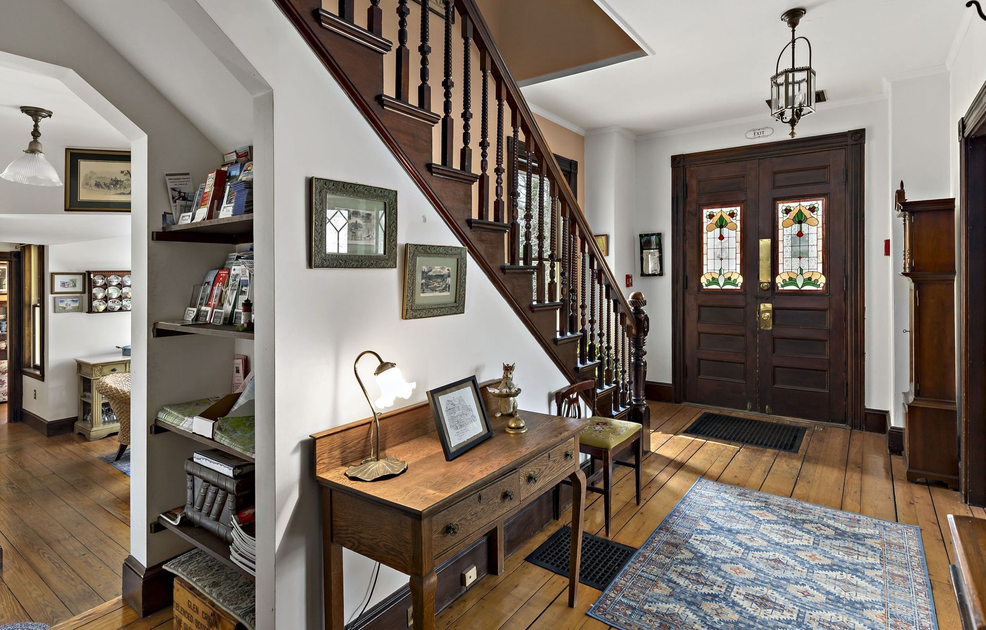 A hallway with a wooden staircase and a wooden desk.