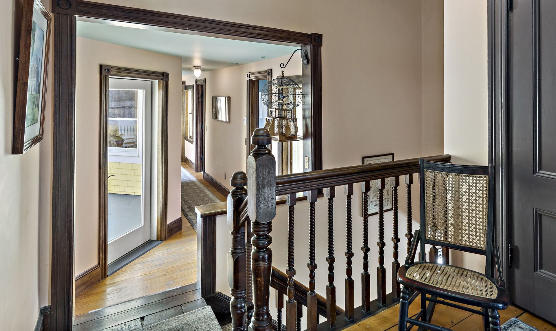 A staircase with a wooden railing and a rocking chair in a hallway.