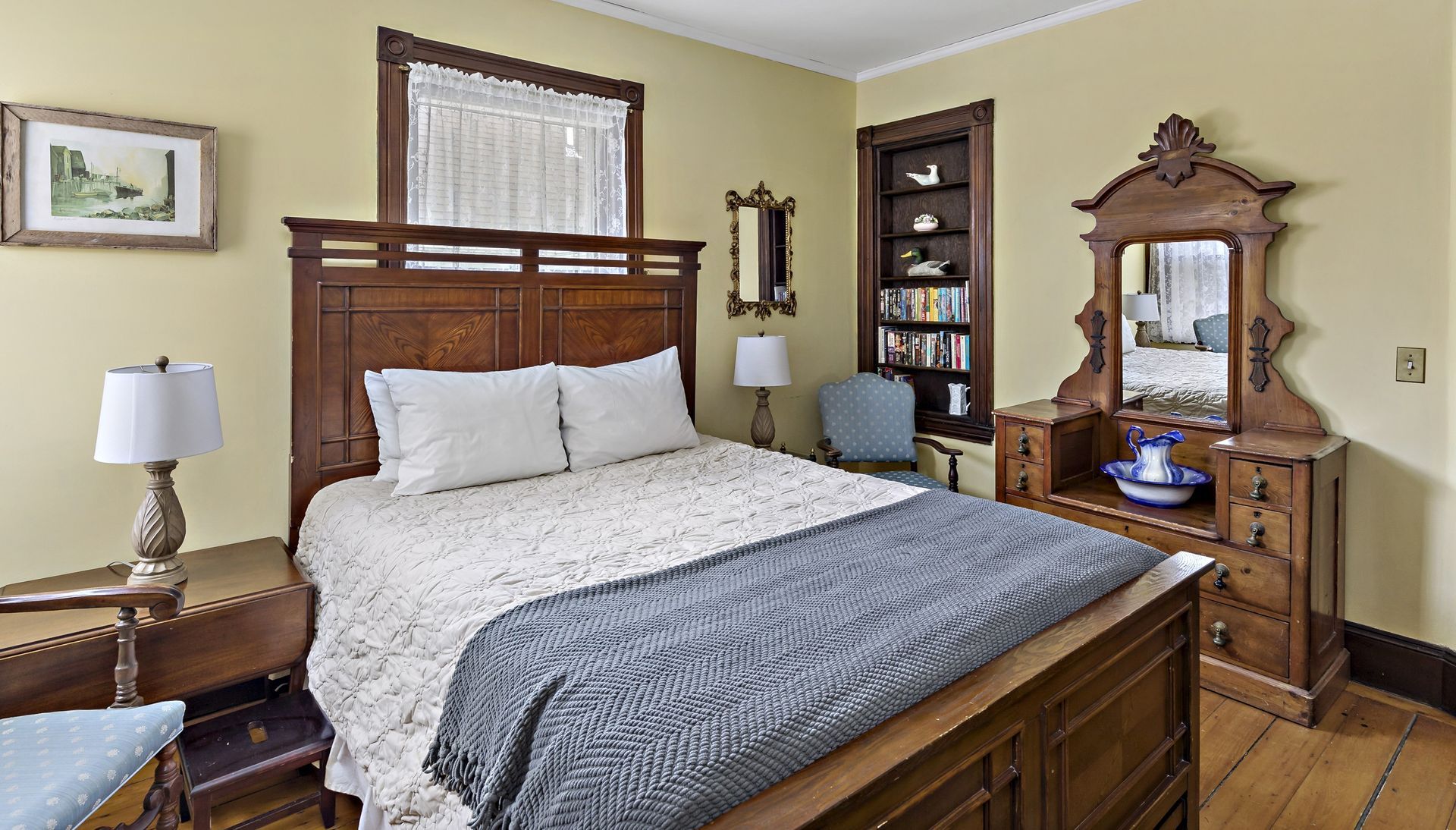A bedroom with a bed , dresser , chair , lamp and mirror.