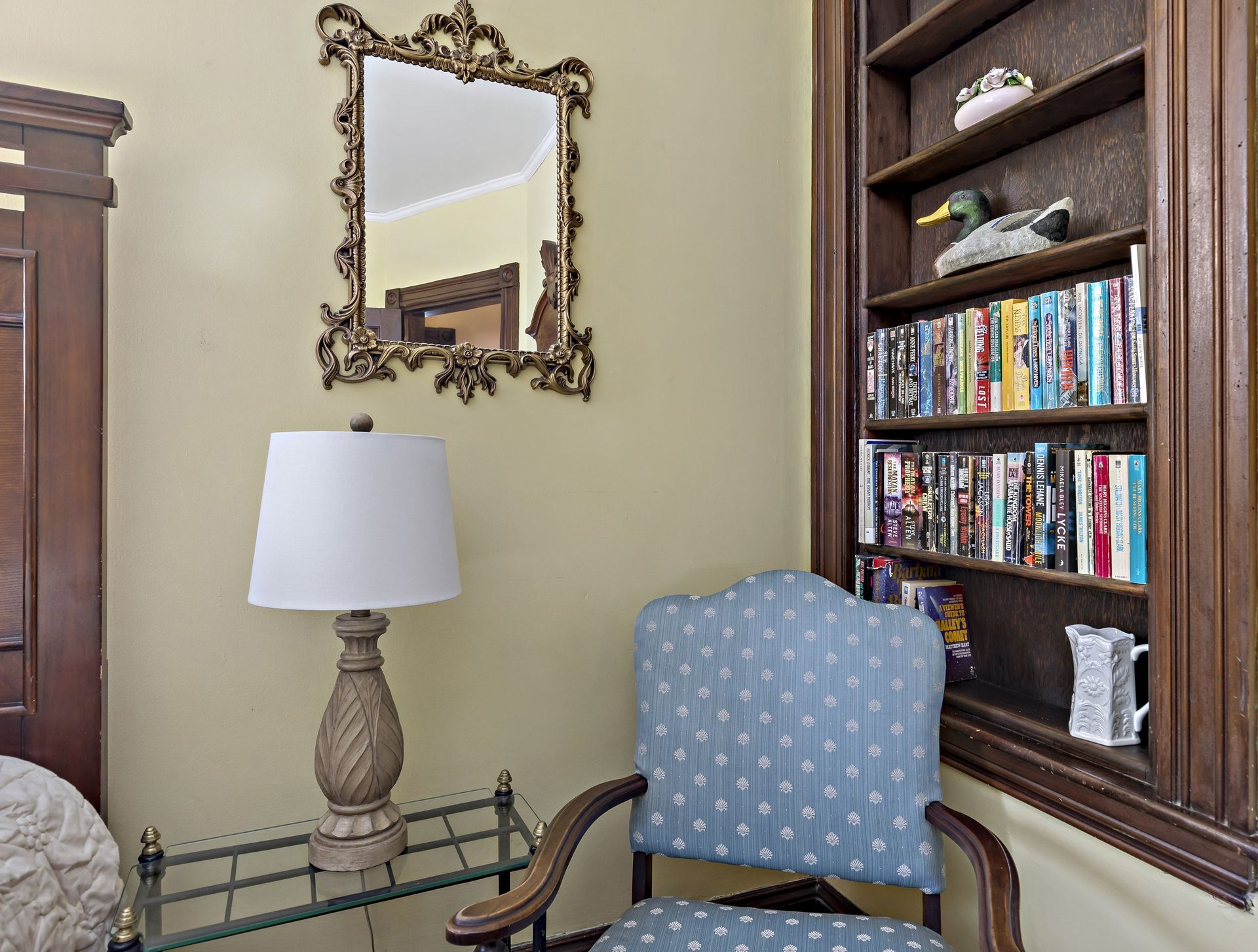 A room with a chair a lamp and a bookshelf