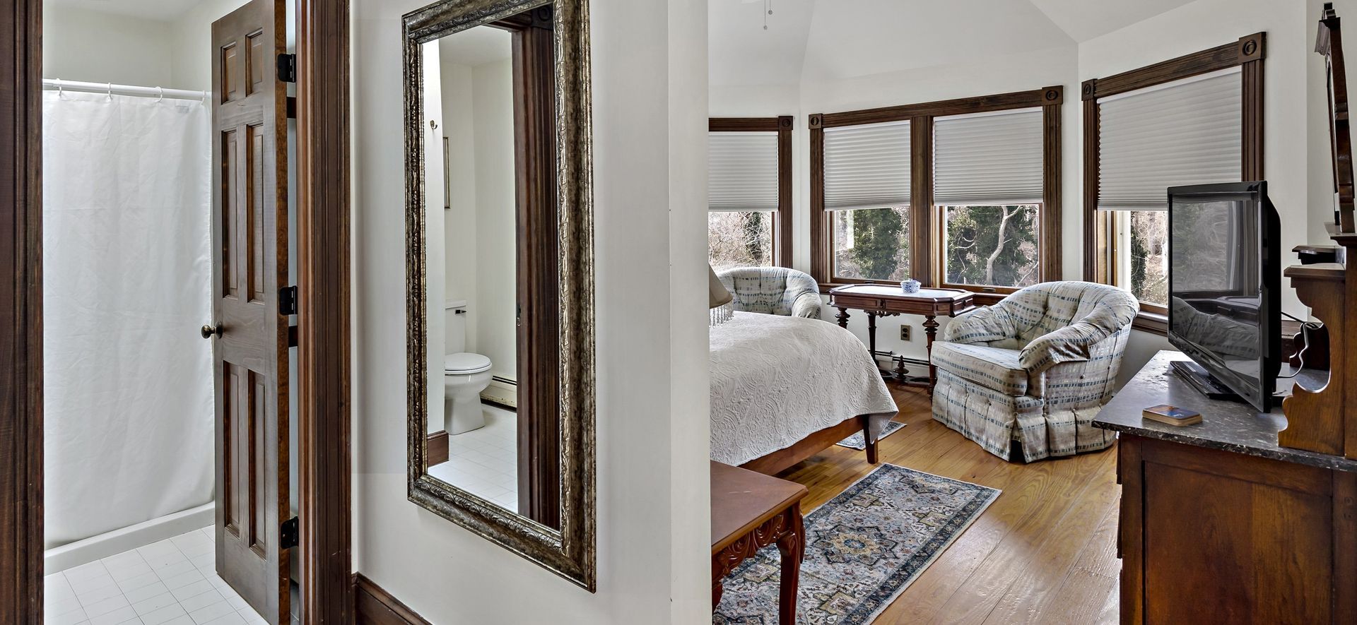 A bedroom with a bed , chair , television and two mirrors on the wall.