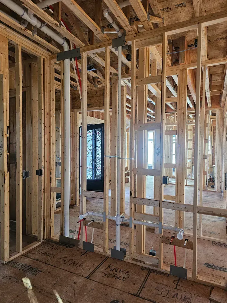 The inside of a house under construction with wooden beams and pipes.