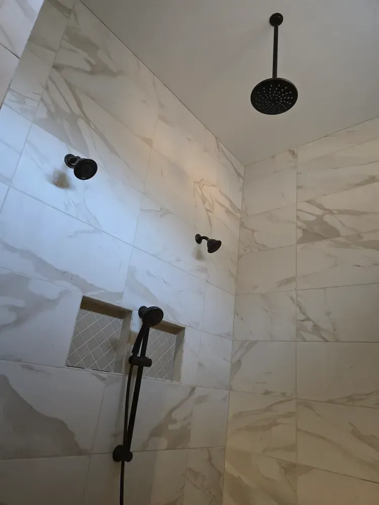 A shower with a black shower head hanging from the ceiling.
