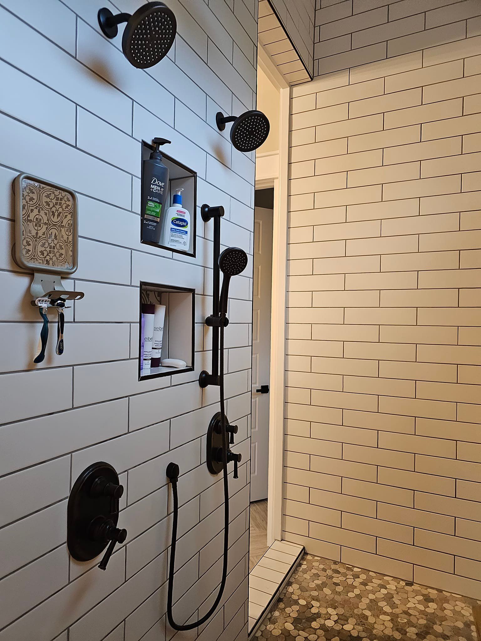 A bathroom with white tiles and black shower heads