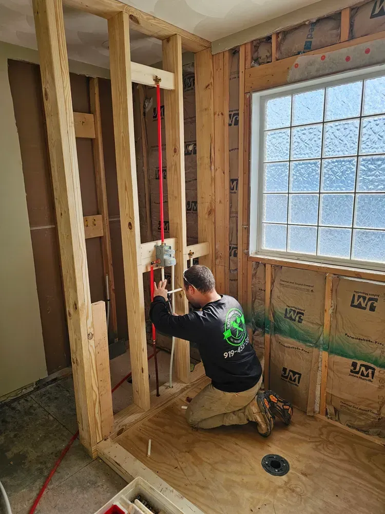 A man is kneeling down in a bathroom while working on a pipe.