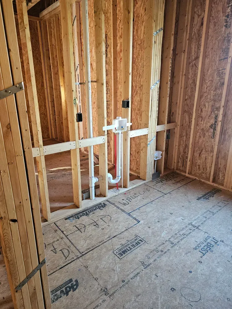 A room in a house under construction with wooden beams and pipes.