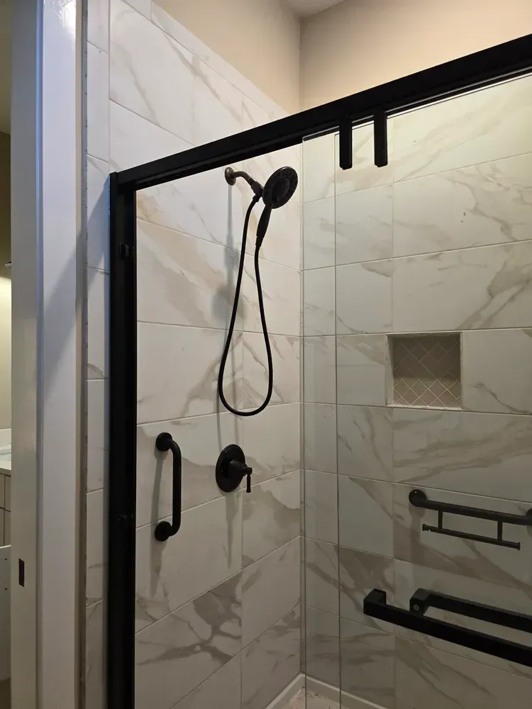 There is a shower with a black frame and a shower head.