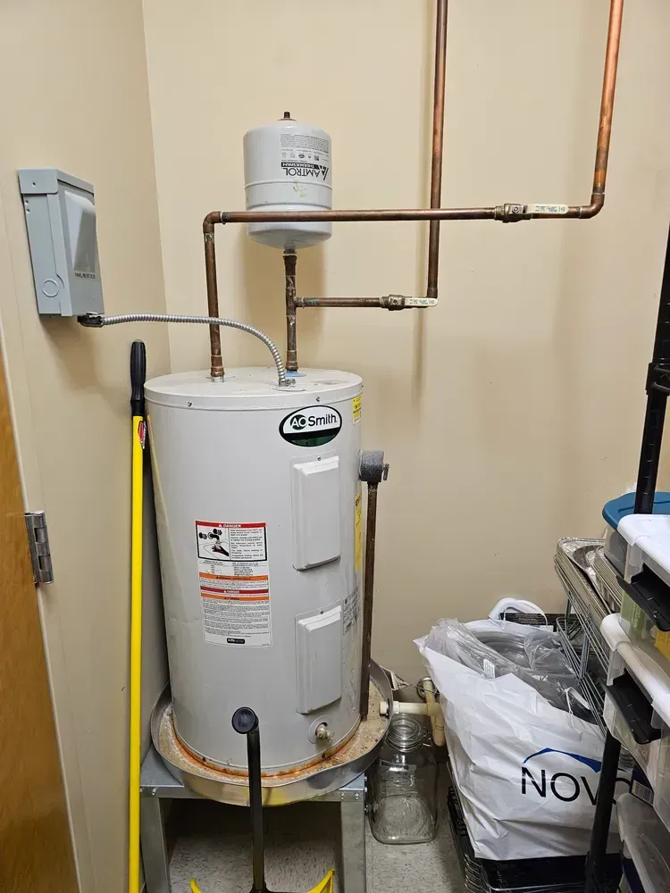 A water heater is sitting in a room next to a mop.